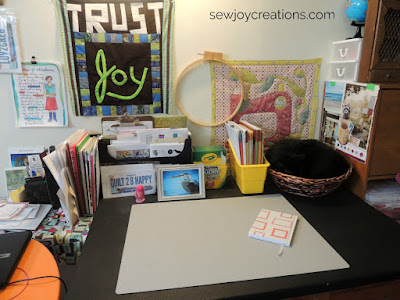 desk with writing supplies and cat basket desk in quilting space with cat in basket